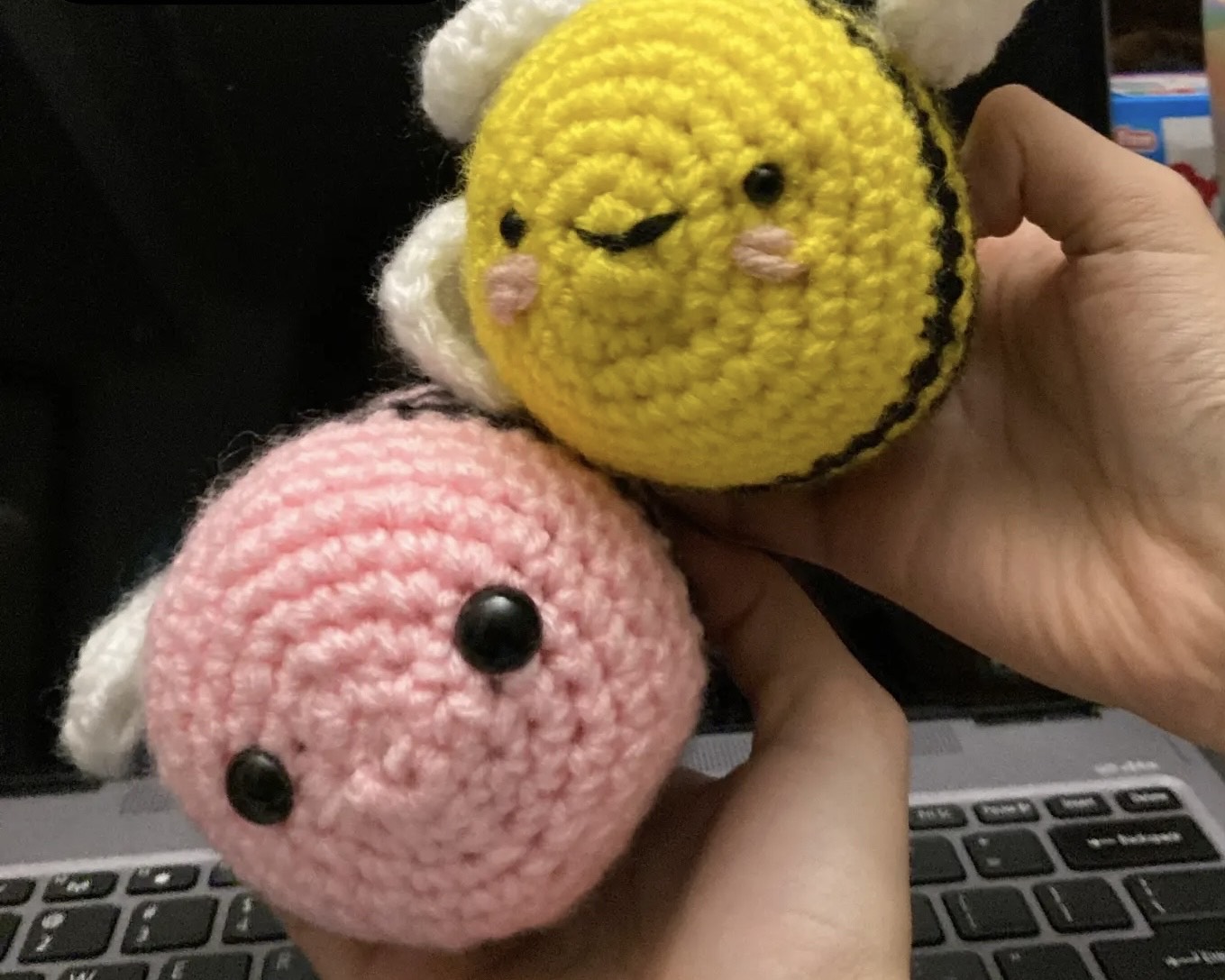 Two hands hold two crochet bees, one pink and one yellow.