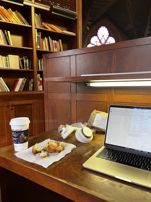 A laptop and a half-eaten croissant on a library cubicle desk