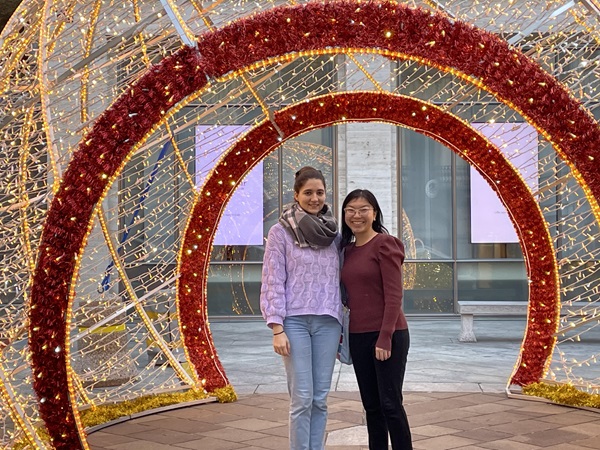 two women stand in an arched Christmas lights display