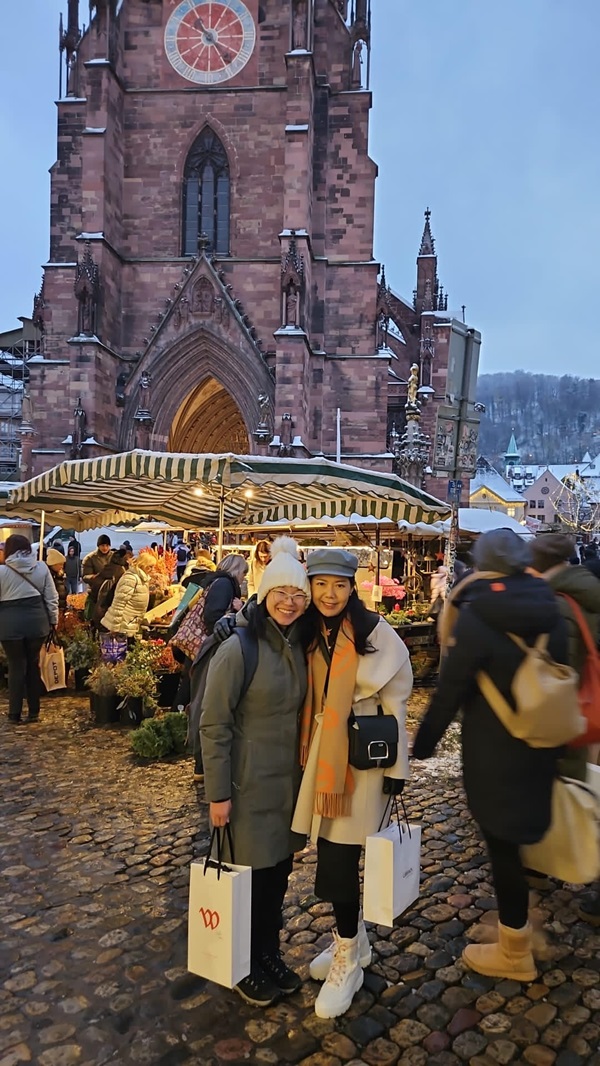Two women pose with shopping bags in a Christmas market