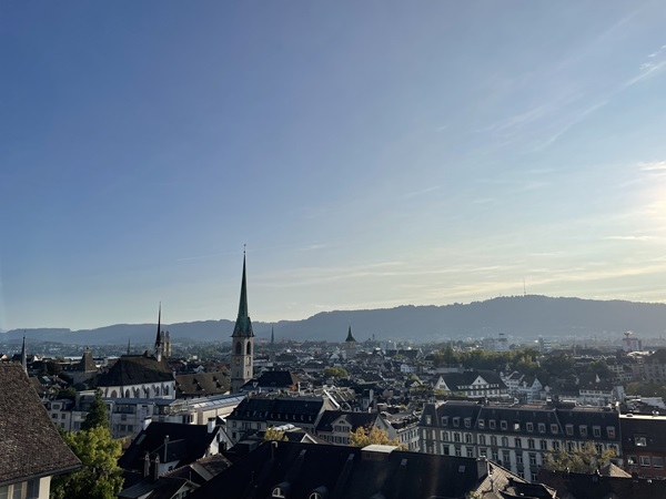 Afternoon view of Zürich from the terrace outside the main building of ETH which includes several church steeples and a hill in the background.