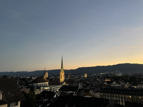 Night-time view of Zürich from the terrace outside the main building of ETH which includes several church steeples and a hill in the background.