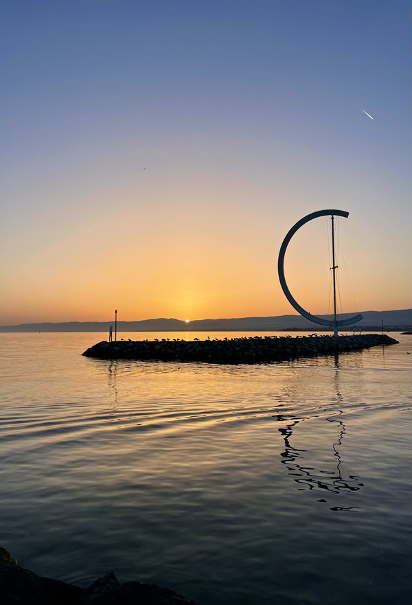 A C-shaped sculpture on a small rock island on Lake Geneva at sunset